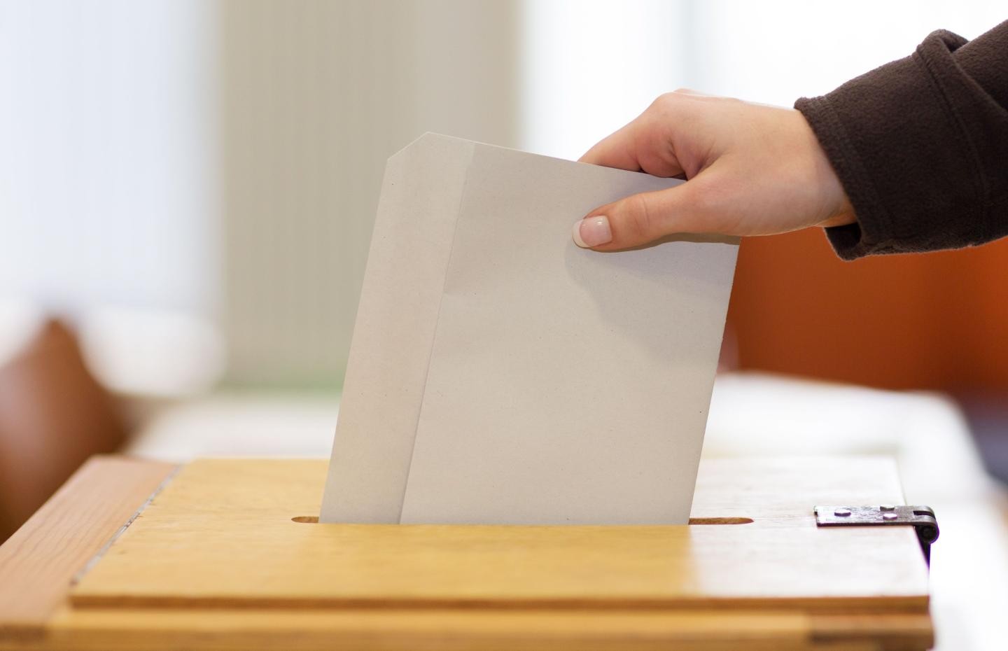 Das Bild zeigt das Einwerfen des Stimmzettels in eine Wahlurne. 