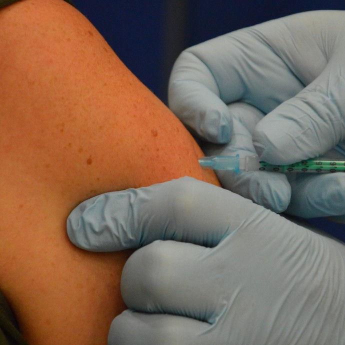 Das Bild zeigt, wie ein Arzt die Impfnadel in den Oberarm einer Person sticht. 