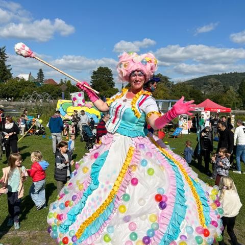 Kinderfest Horbachpark Eine lächelnde Stelzenläuferin oder Entertainerin in einem ausladenden, bunten Kostüm, das mit vielen farbigen Bällen dekoriert ist, auf einem Sommerfest.
