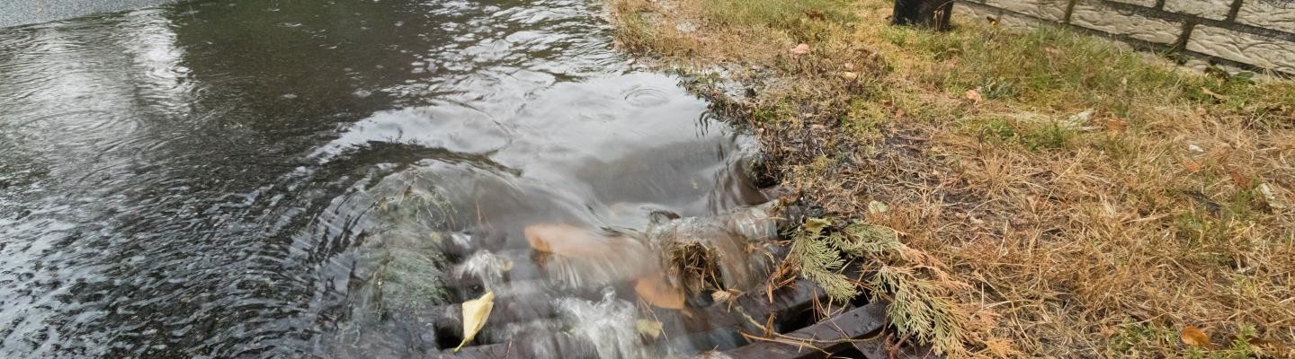 Straße, die mit Wasser überflutet ist. Das Wasser läuft in einen Gulli. Straße, die mit Wasser überflutet ist. Das Wasser läuft in einen Gulli.