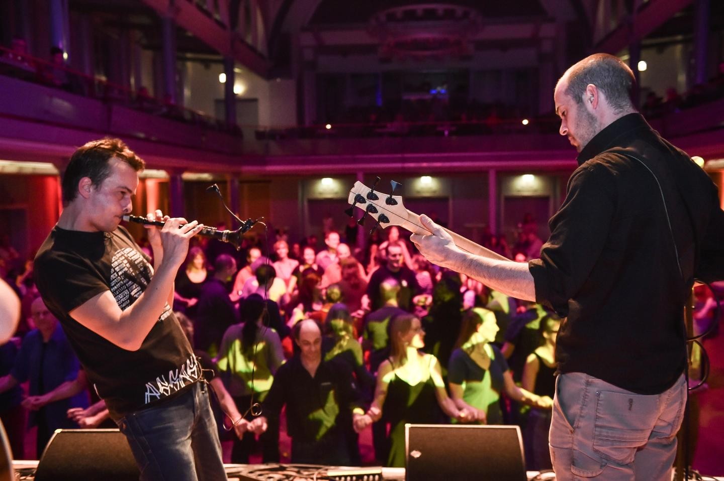Zwei Musiker im Vordergrund, einer spielt Gitarre, der andere Klarinette; im Hintergrund tanzendes Publikum