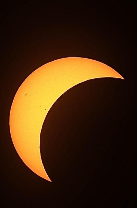 Sonnenfinsternis partiell Nahaufnahme einer partiellen Sonnenfinsternis: Die Sonne ist als leuchtend orange-gelbe Sichel vor einem tiefschwarzen Hintergrund zu sehen. Auf der Oberfläche der Sonnensichel sind kleine, dunkle Sonnenflecken erkennbar
