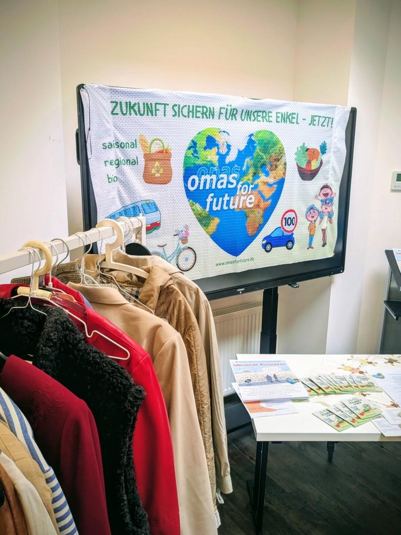 Kleiderständer, im Hintergrund Omas for Future Plakat