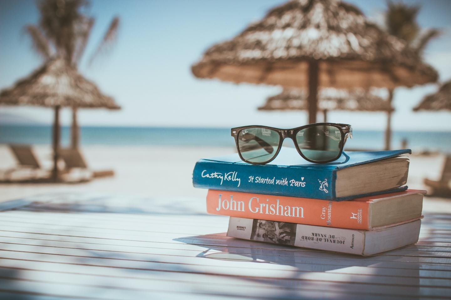 drei Bücher und eine Sonnenbrille liegen auf einem Tisch am Strand 