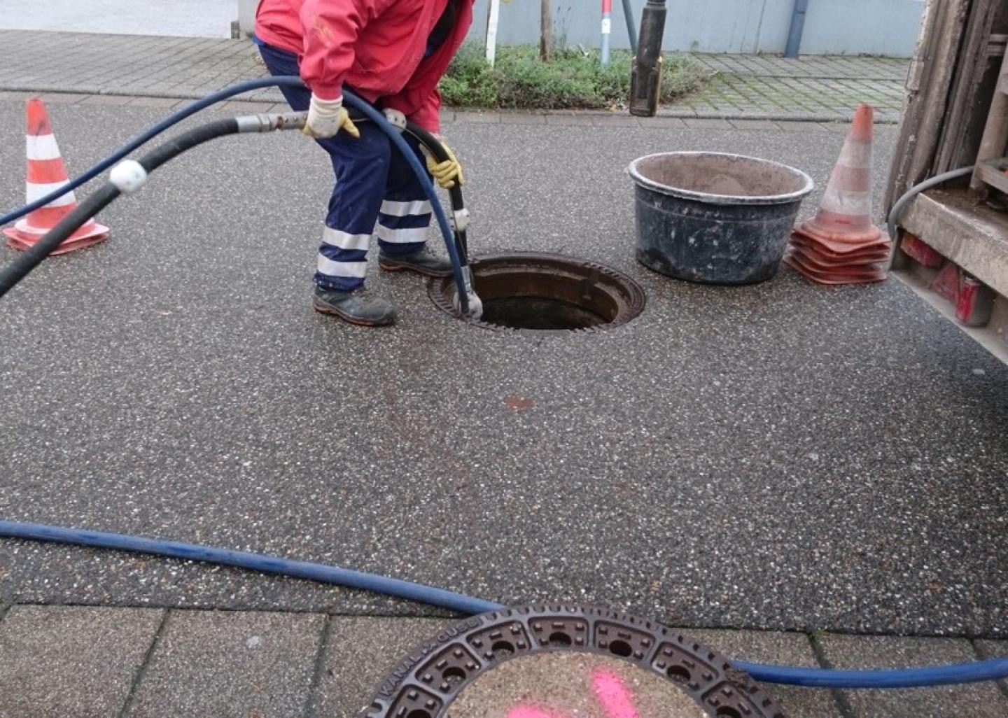 Arbeiter beim Einbringen von zwei Kabeln in Kanalschacht
