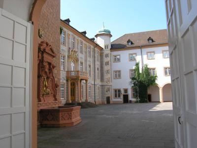 Das Bild zeigt einen Innenhof des Barockschloss Ettlingen mit historischen Gebäuden und einem Brunnen mit Delphin-Motiv. Schlosshof mit prunkvollen Außenfassade und vergoldetem Dephinbrunnen