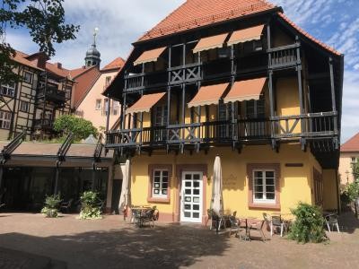 Das Bild zeigt den Weißenberger Hof, ein historisches Fachwerkgebäude mit gelber Fassade und schwarzem Holzgebälk. Im Vordergrund sind Tische und Stühle auf dem Platz zu sehen. Der Weißenberger Hof, Fachwerkhaus