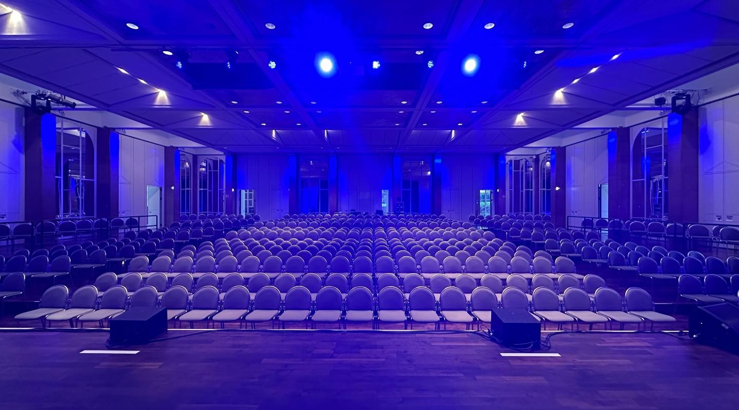 Innenansicht der Schlossgartenhalle mit blauer Beleuchtung und abgesenktem Saal frontale Sicht von Bühne aus