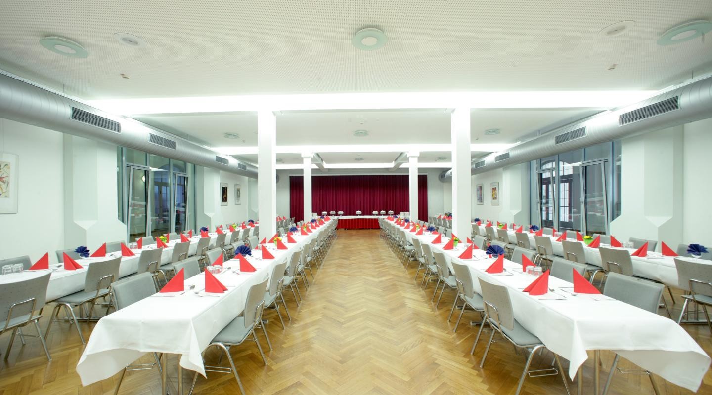 Bürgerkeller der Stadthalle mit Langtischen, weißen Tischdecken und roten Servietten