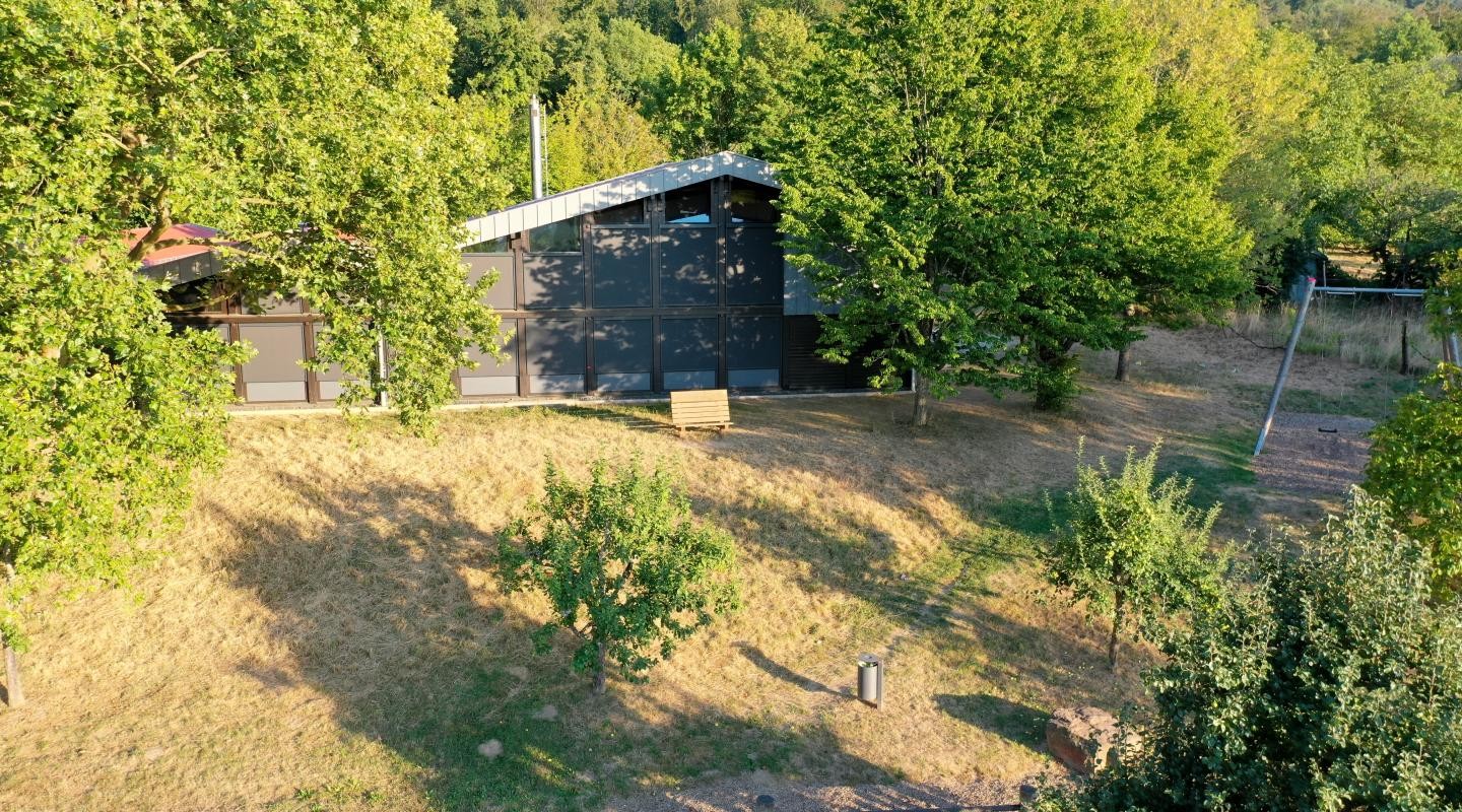Waldsaumhalle Außenansicht mit Verdunklungsanlage mit grünen Bäumen und Bewegungspfad
