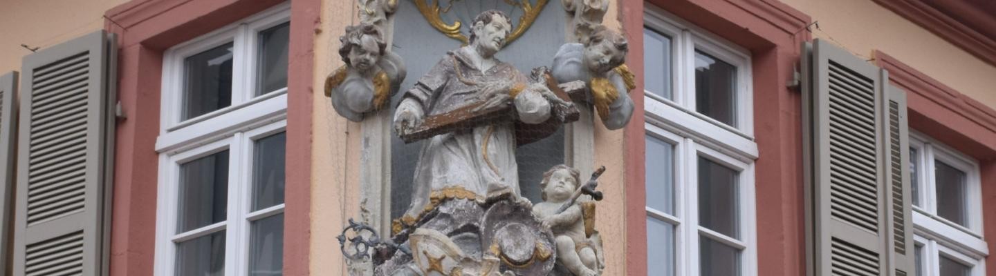 Mann hält ein Kreuz in seinen Armen und wird von zwei Engeln begleitet