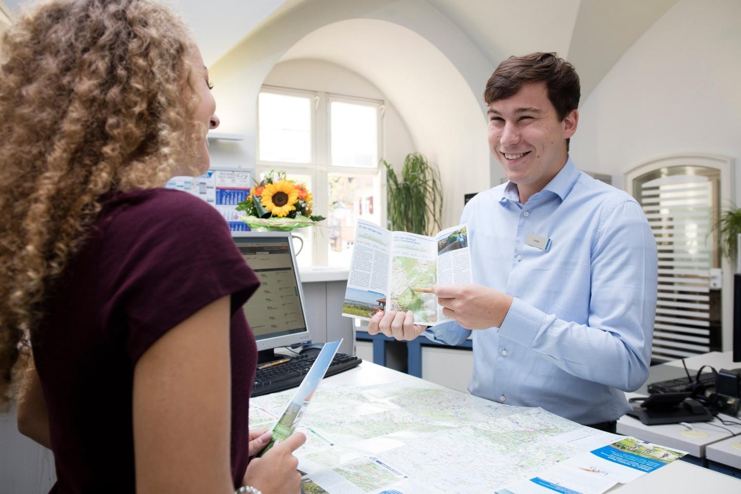Eine junge Frau informiert sich bei einem Mitarbeiter der Stadtinformation über Wanderwege.