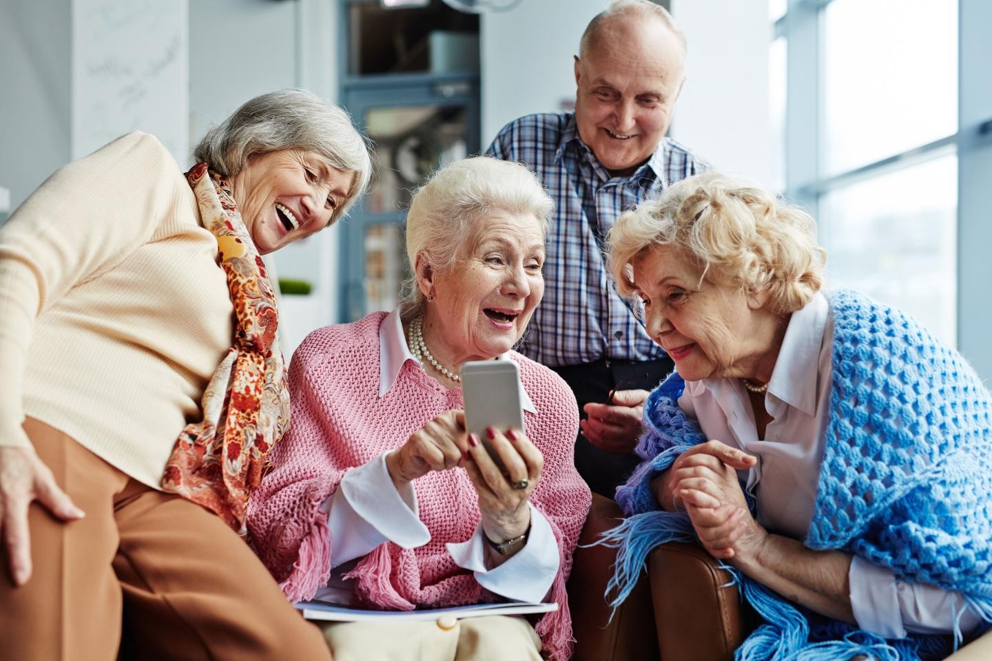 Zu sehen sind vier Senioren, die über irgendwas auf dem Handy einer der Damen lachen.