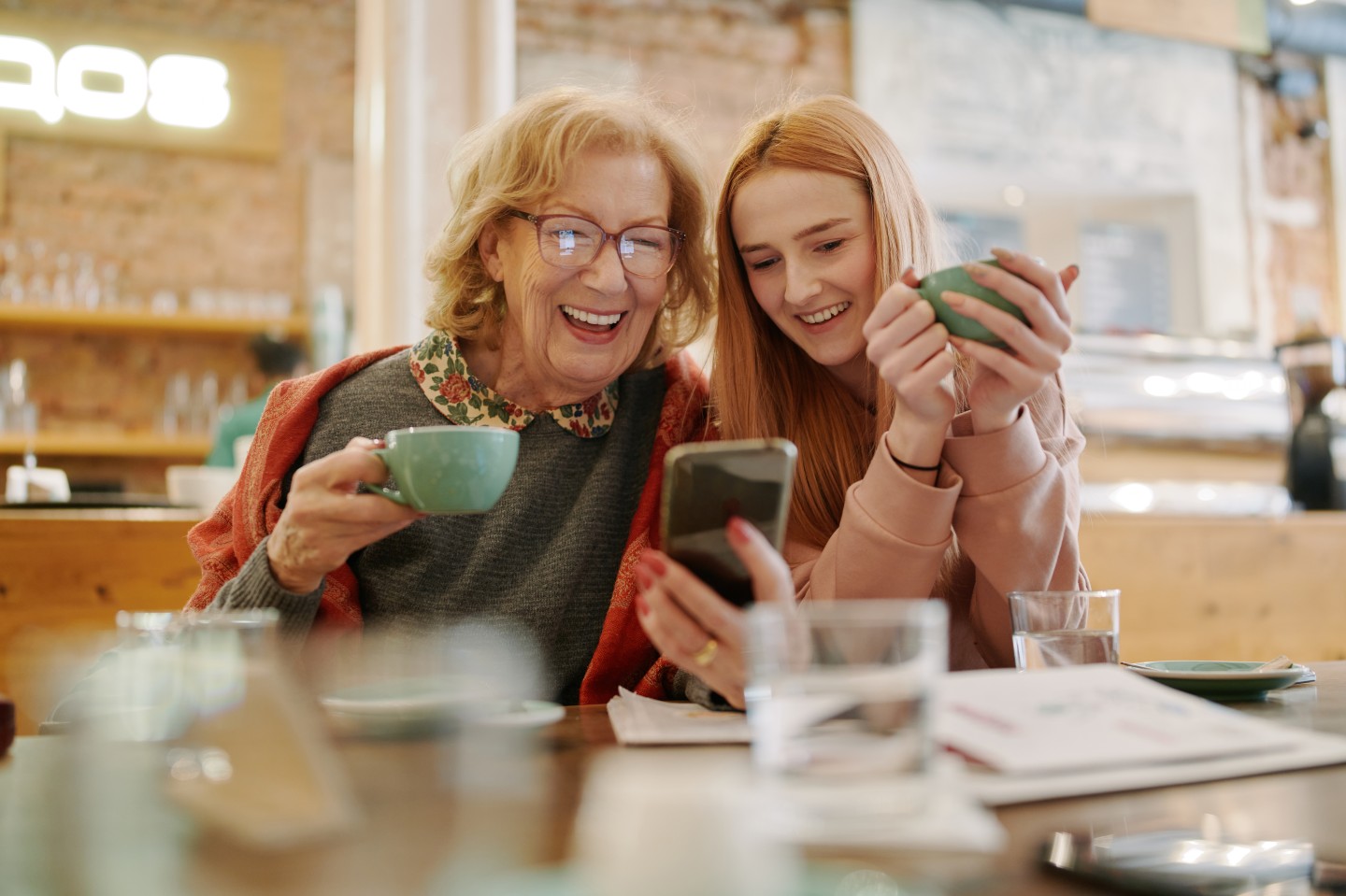Bild zeigt Seniorin mit Smartphone in der Hand und Jugendliche 