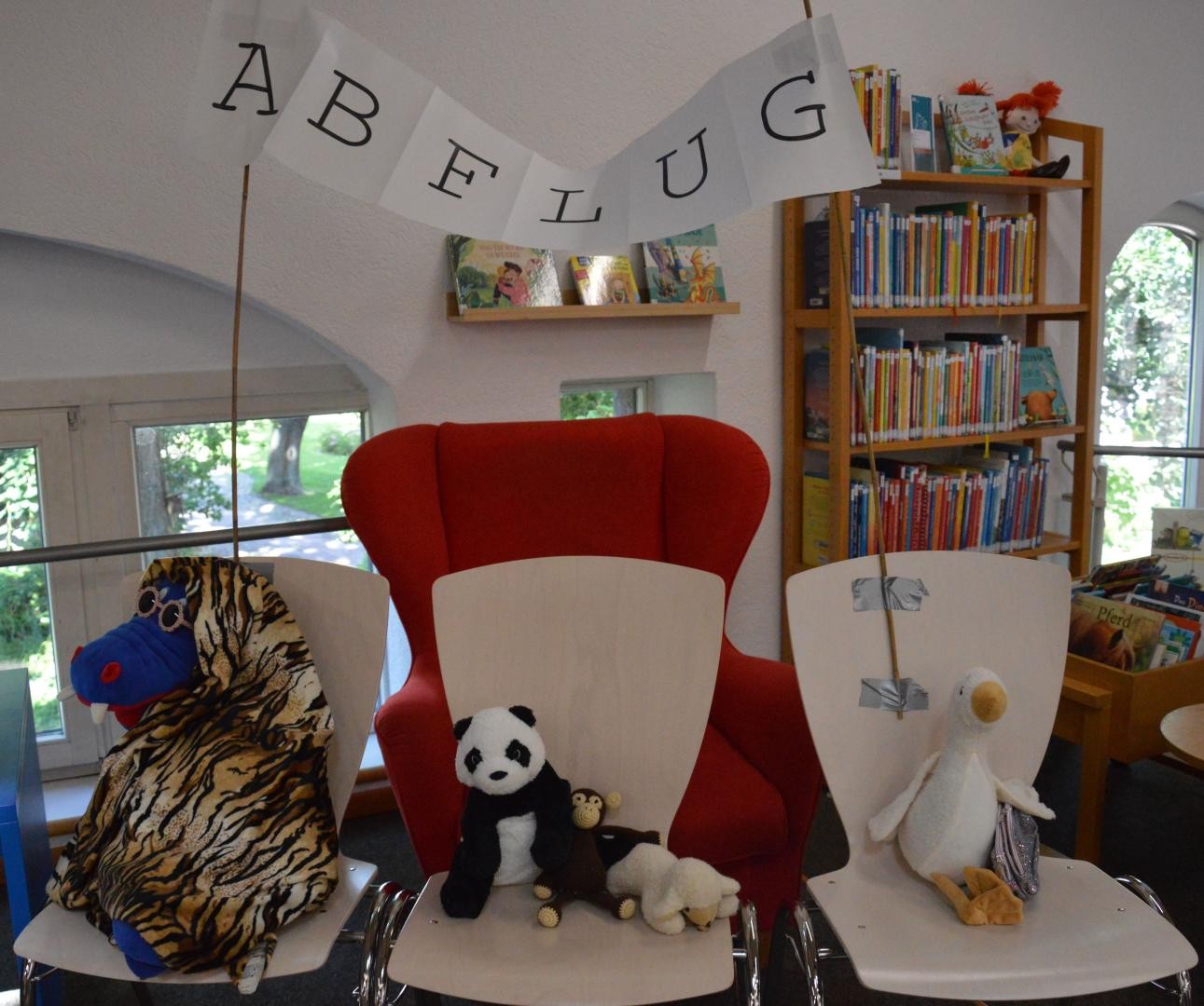 Auf Stühlen verteilt sitzen eine Gans, ein Äffchen, zwei Schafe, ein Pandabär und ein Tiger