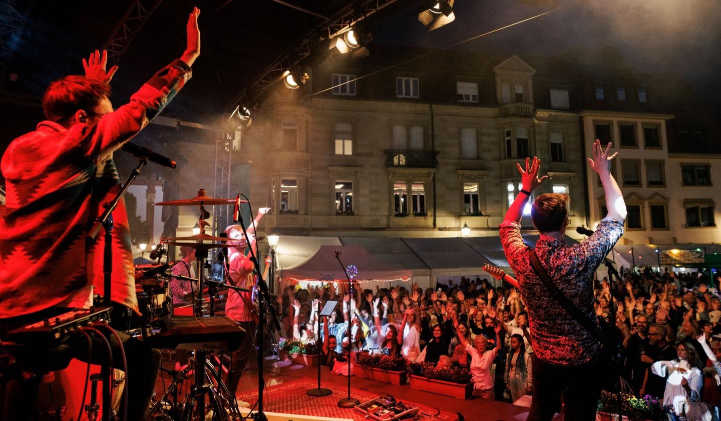 Marktfest 2025 Blick von der Bühne Erwin-Vetter-Platz in die Menge, Bandmitglieder mit erhobenen Händen, rotes Licht.