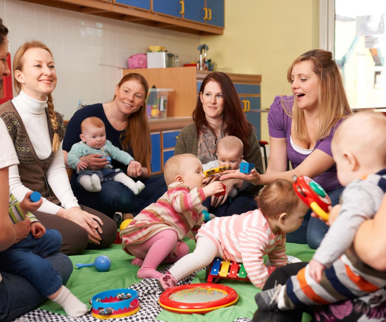 Junge Frauen sitzen im Kreis, in der Mitte spielen ihre Babys