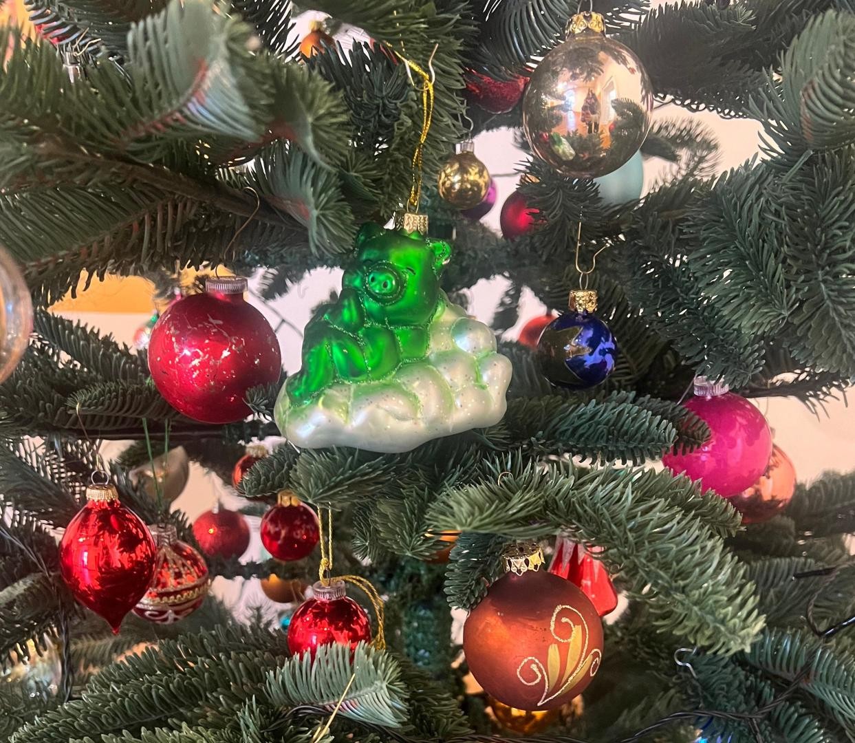 Ein Bildausschnitt eines geschmückten Weihnachtsbaums, im Zentrum ein grünes Glücksschwein