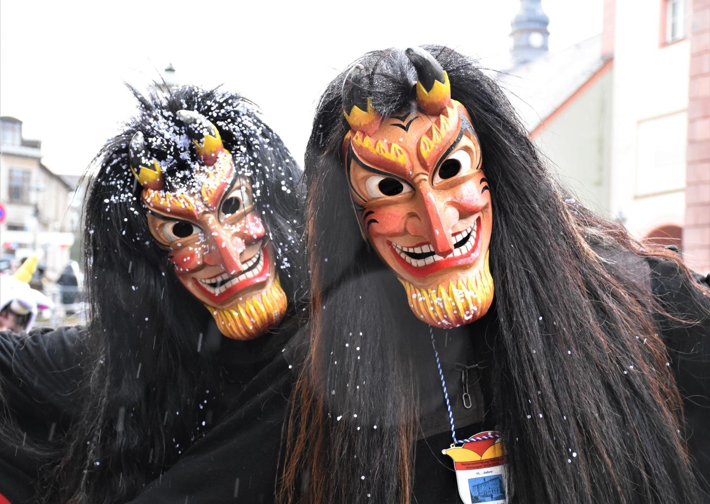 Zwei Teufel im Häs und mit Larve, auf der teilweise Konfetti liegt 