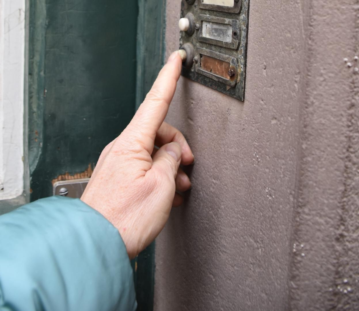 Ein altes Klingelschild, eine Hand drückt den Klingelknopf