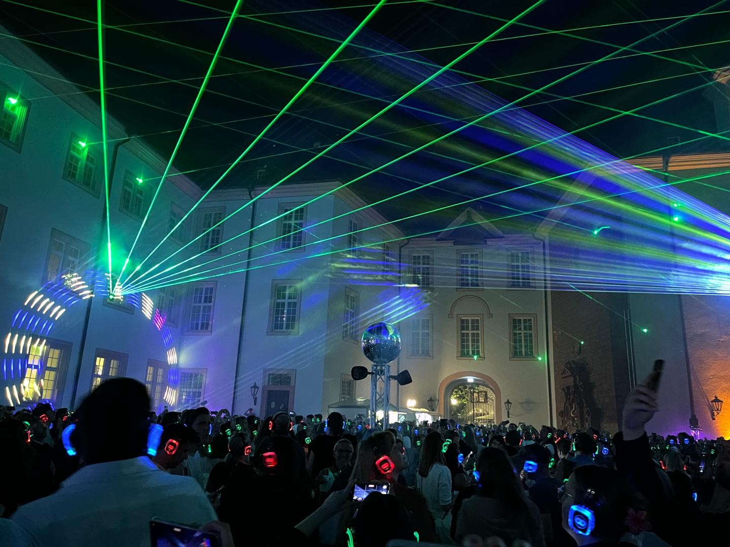 Feiernde mit blinkenden Kopfhörern und eine Lichtshow im Schlosshof