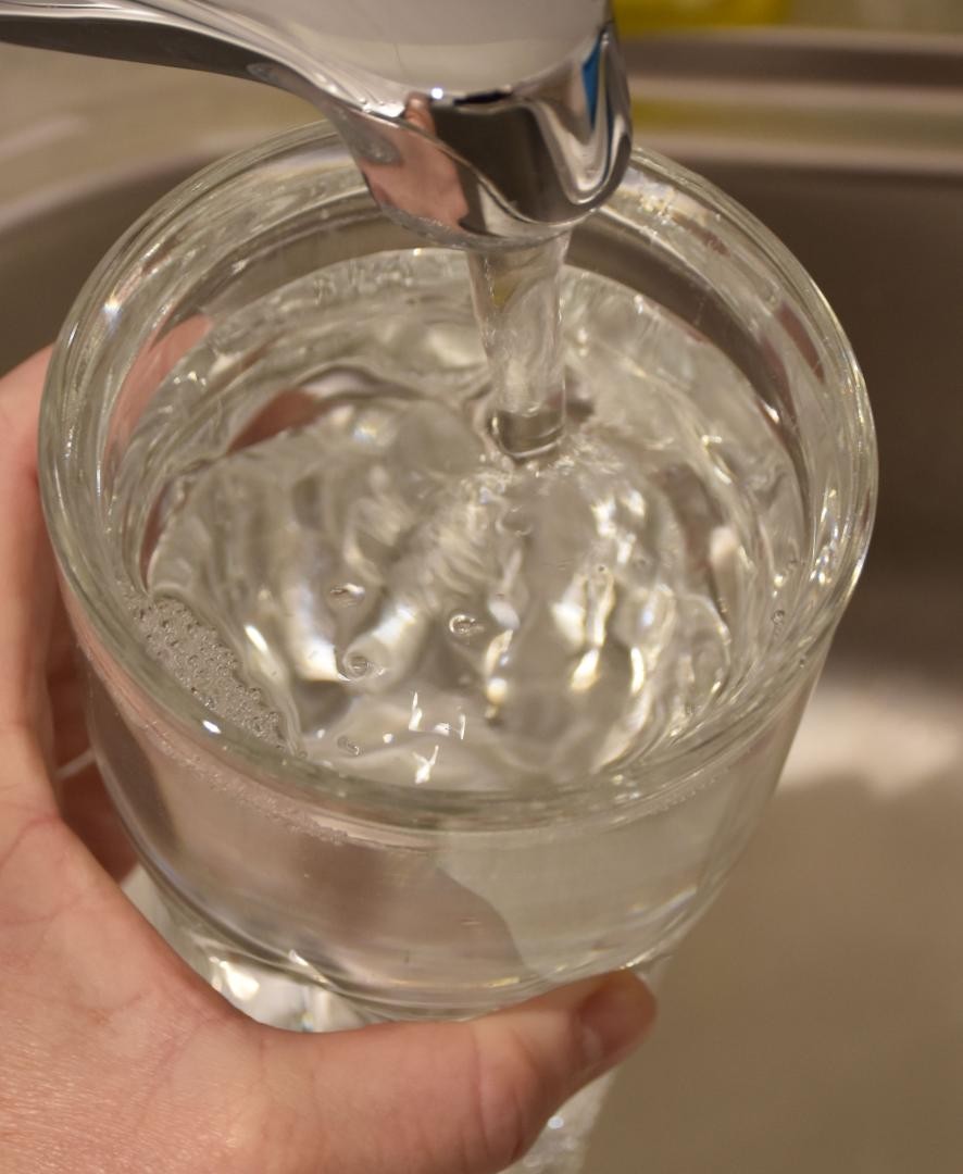 Wasser aus dem Hahnen fließt in ein Glas. 