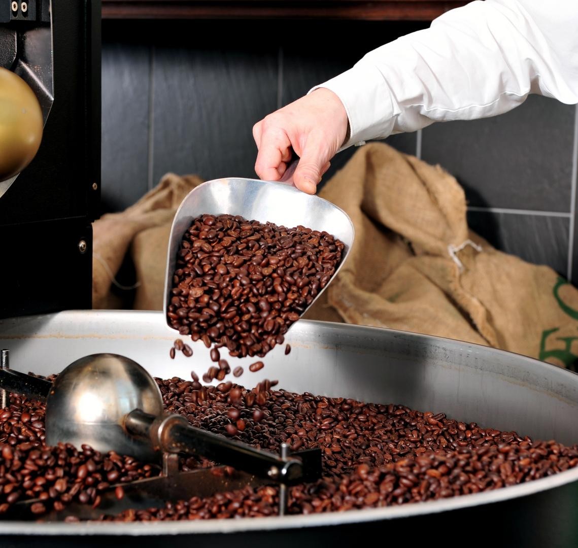 Walk and Talk am 26. September: Fairer Kaffee Symbolbild Adobe Stock: ein Kaffeeröster schüttet Kaffee in eine Rösttrommel- Man sieht nur den Arm mit der Schüttel
