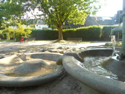 Wasserpumpstation mit darunterliegenden kleinen Wasserbecken, über die Wasser in Sandspielfläche läuft