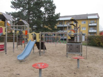 zwei Kletterspielgeräte links und rechts Kleinrutsche in der Mitte auf Sandspielfläche