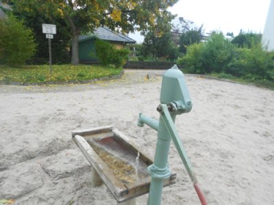 Handwasserpumpe mit kleinem darunterliegendem Holzauffangbecken auf Sandspielfläche