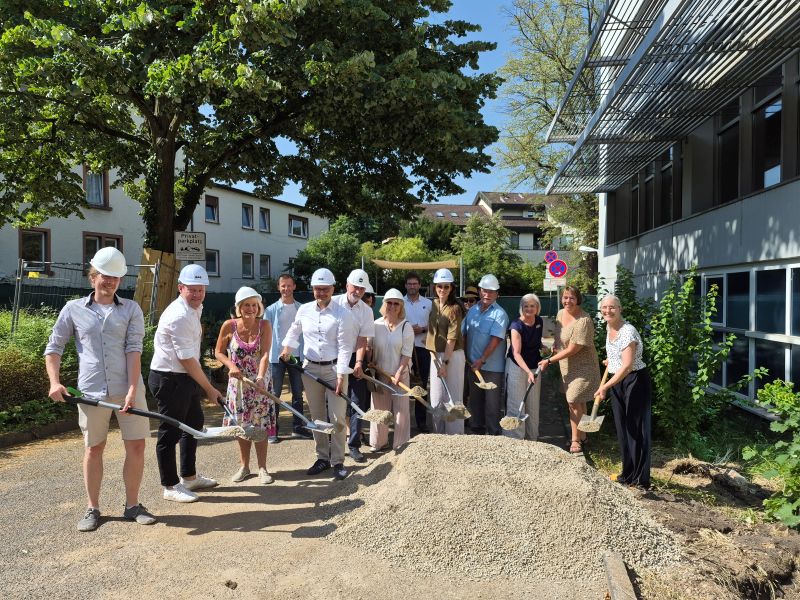 Projektbeteiligte stehen mit Schaufeln an der zukünftigen Baustelle
