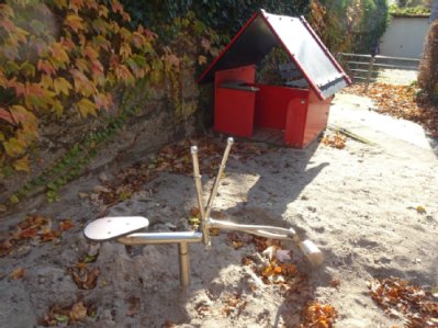 im Vordergrund stilisierter Minibagger zum Sand Baggern im Hintergrund Spielhütte für Kleinkinder