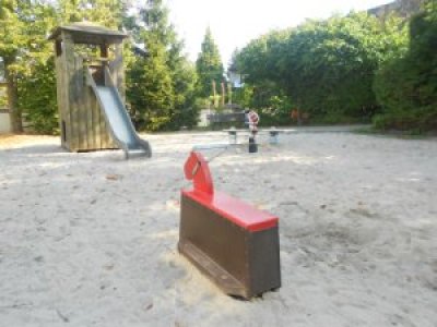 Im Vordergrund Wipppferd, im Hintergrund Rutschturm, auf Sandspielfläche
