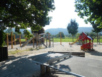 Tischtennisplatte im Vordergrund, Klettergeräte und Rutsche im Hintergrund auf Sandspielfläche