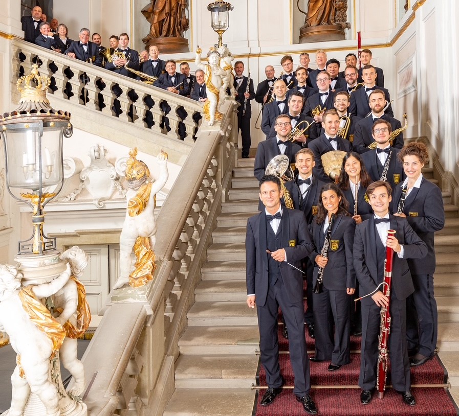 39 Frauen und Männer auf einer Treppe stehen zum Teil mit ihren Instrumenten.