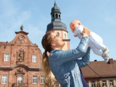 Mutter die ihr Baby hochhebt.Im Hintergrund historisches Rathaus Ettlingen