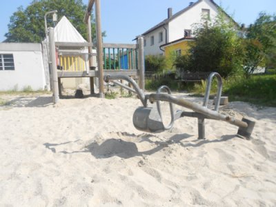 Stilisierter Minibagger auf Sandspielfläche, im Hintergrund Klettergerät