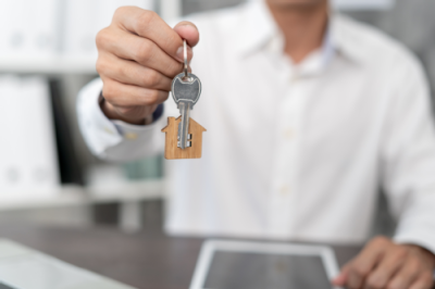 Das Foto zeigt eine Person die einen Schlüssel zu einer neuen Immobilie übergibt.